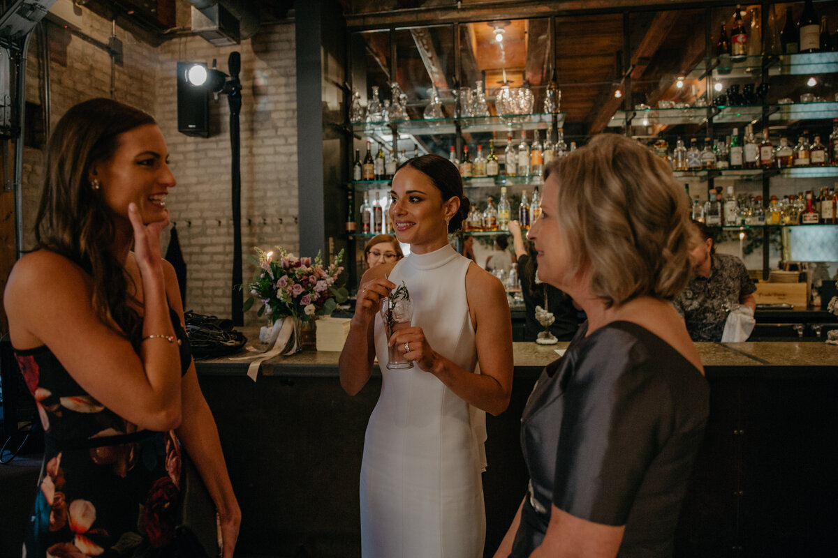 Bride enjoying a drink by the bar laughing with wedding guests