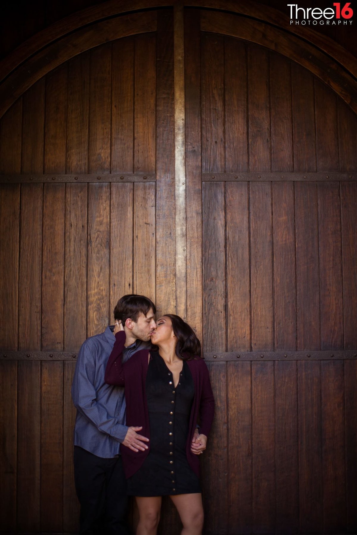 Engaged couple share a romantic kiss in front of large wooden door at the Villa Del Sol