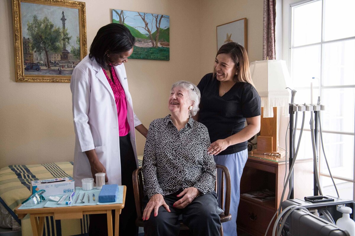 A brand marketing shot of a dentist and her assistant consulting a smiling patient for in home dentistry services shot at a senior care facility in San Diego, CA