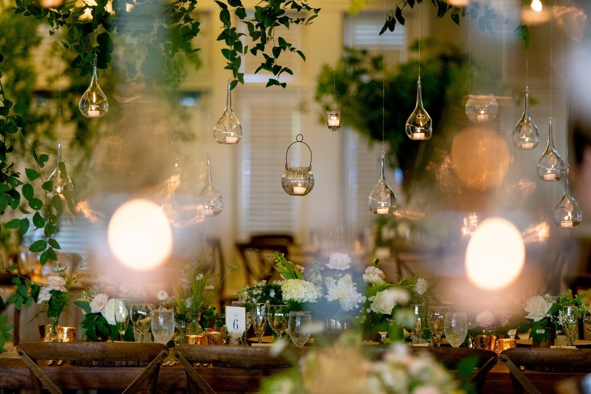 suspended glass candles above each reception guest table with greenery centerpieces
