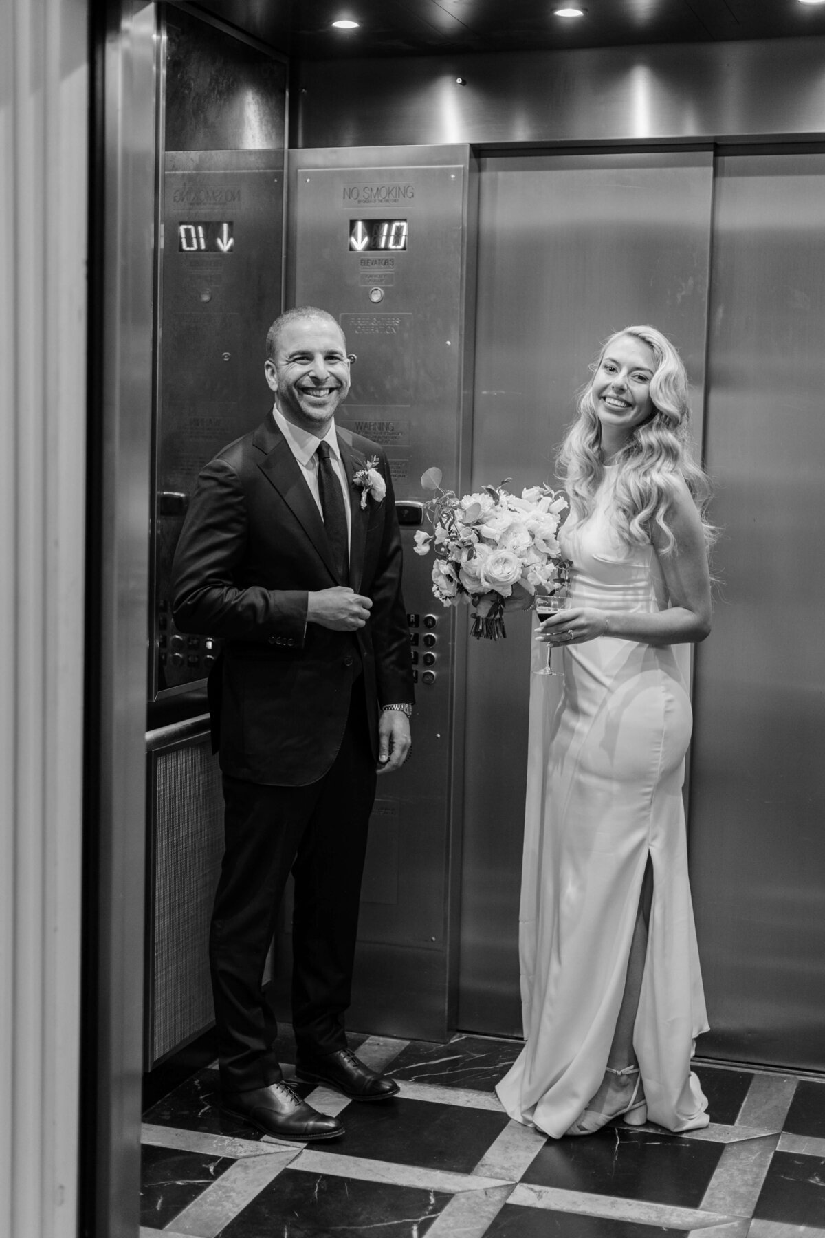 A bride and groom smile in an elevator.