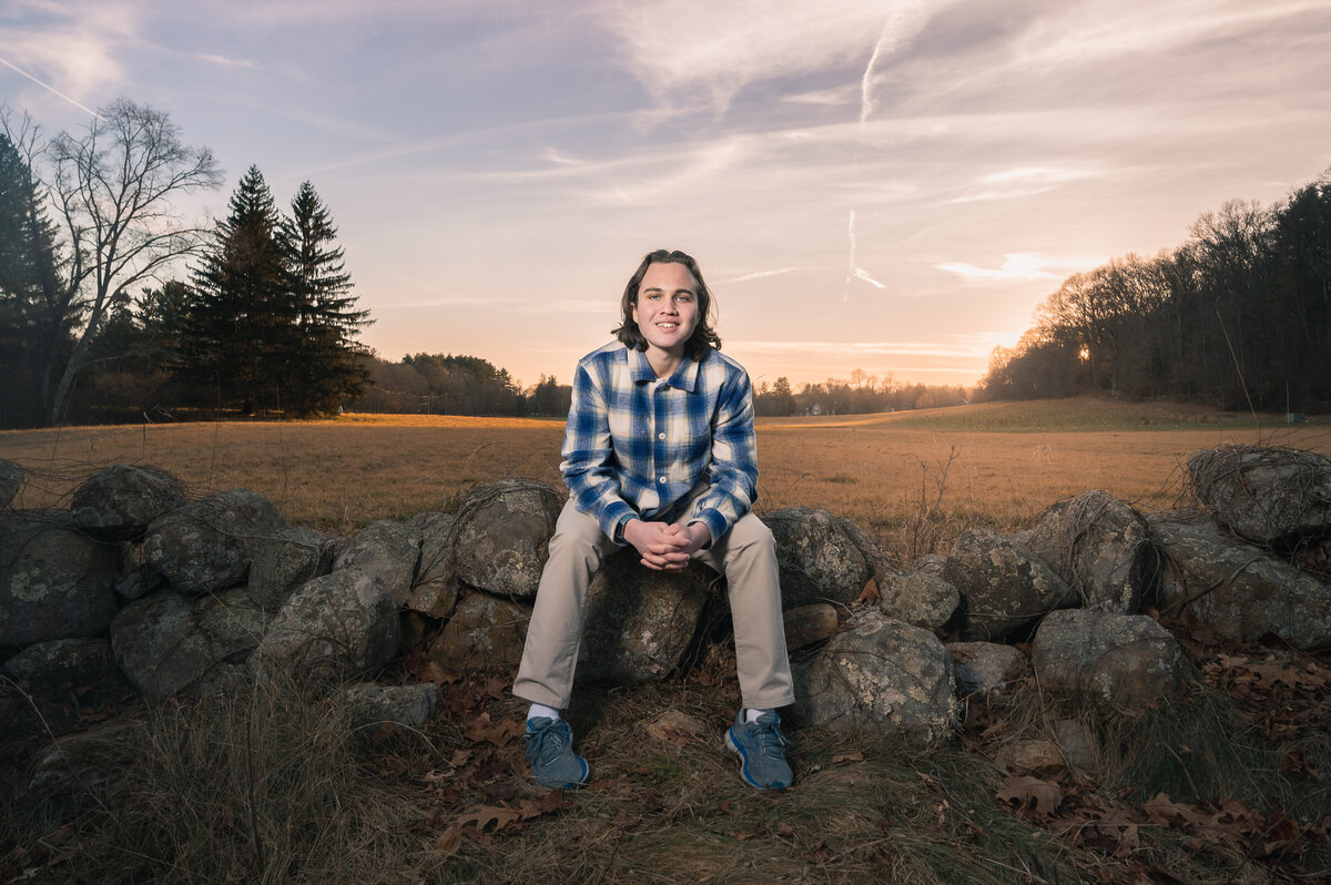 Boston senior portrait sitting on stone wall  with sunset and trees in background