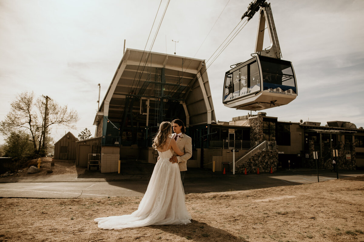 bride and groom standing together with sandia peak tram above them