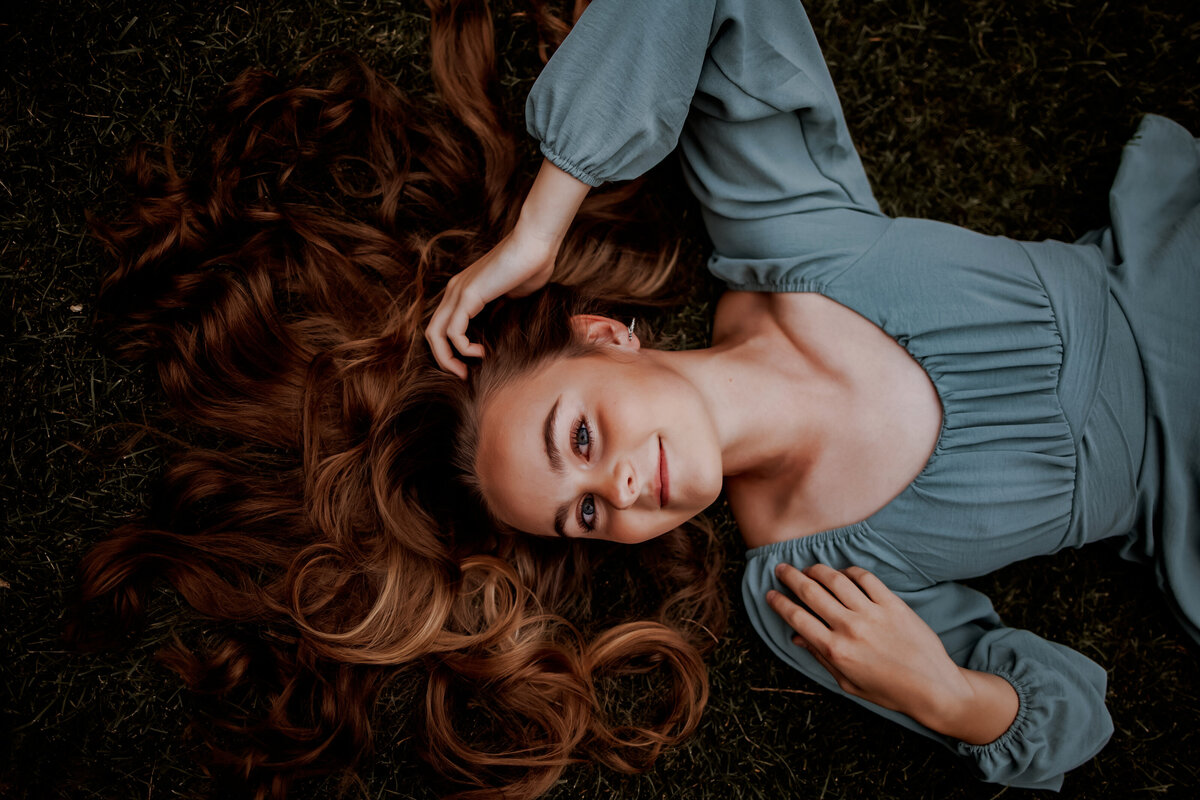 high school girl lays on her back in grass looking up at camera