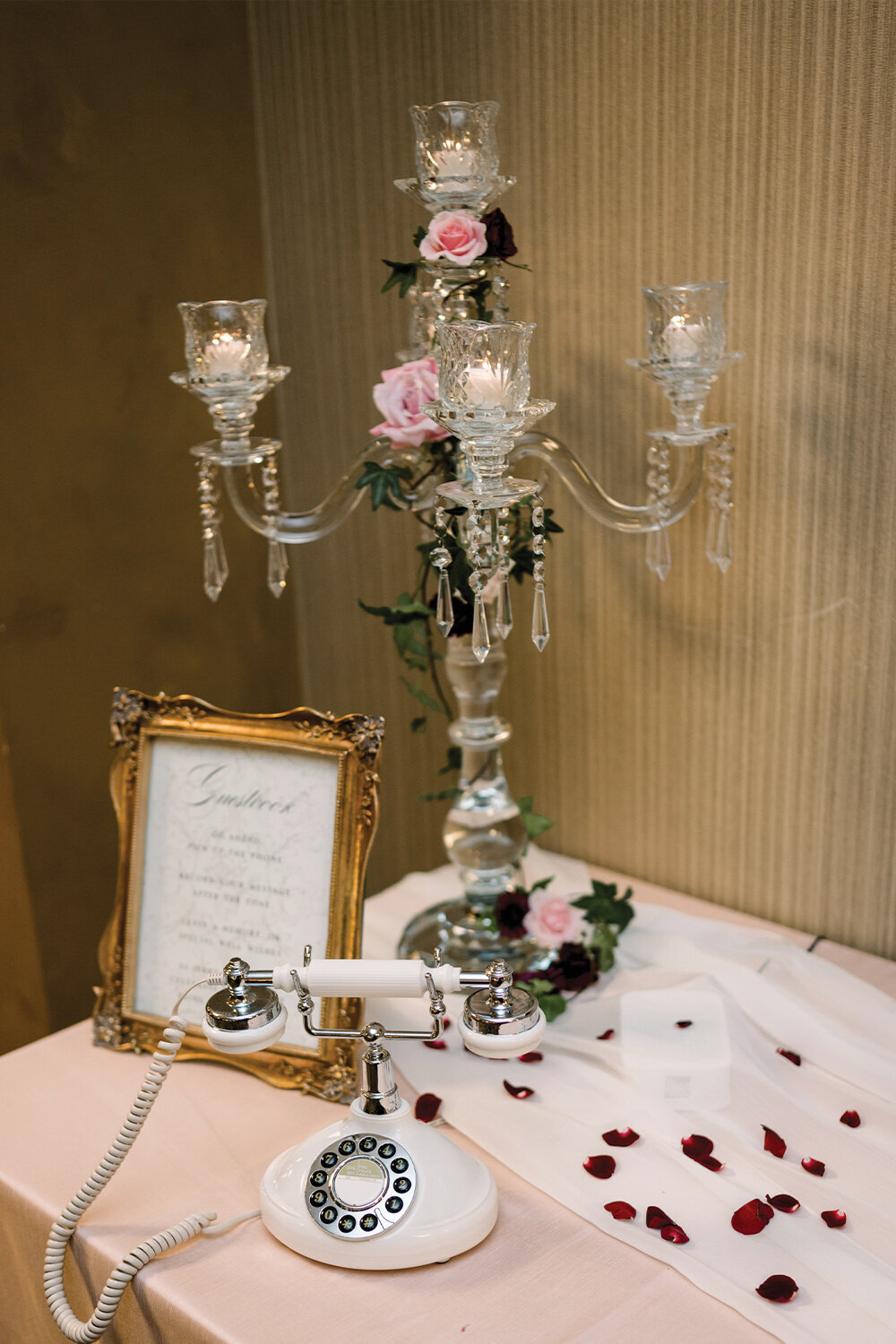 Vintage phone used for an audio guest book on a blush linen table with a crystal candelabra and cascading burgundy and blush florals, complemented by a sheer white table runner.