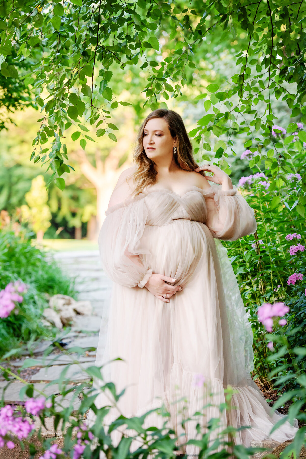 st-louis-maternity-photographer-pregnant-mother-in-flowy-white-gown-holding-belly-standing-in-garden