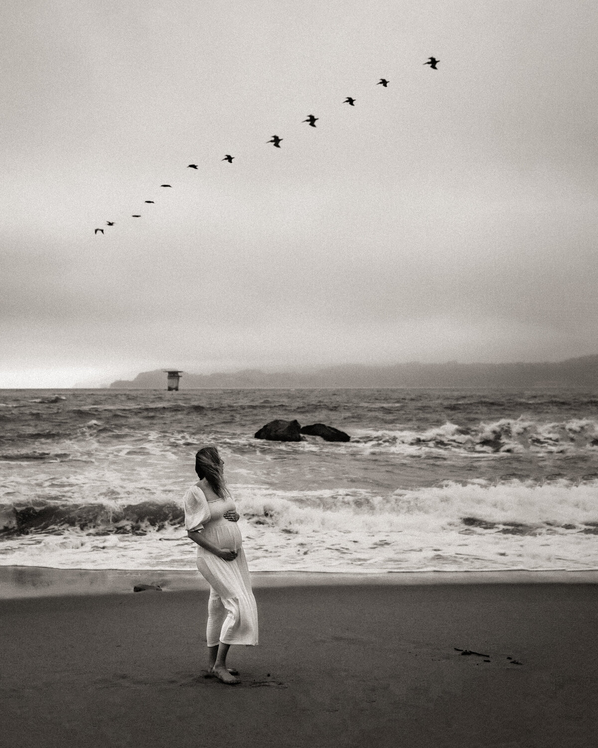San Francisco maternity Mom looks out toward ocean and hold pregnant belly while birds fly above
