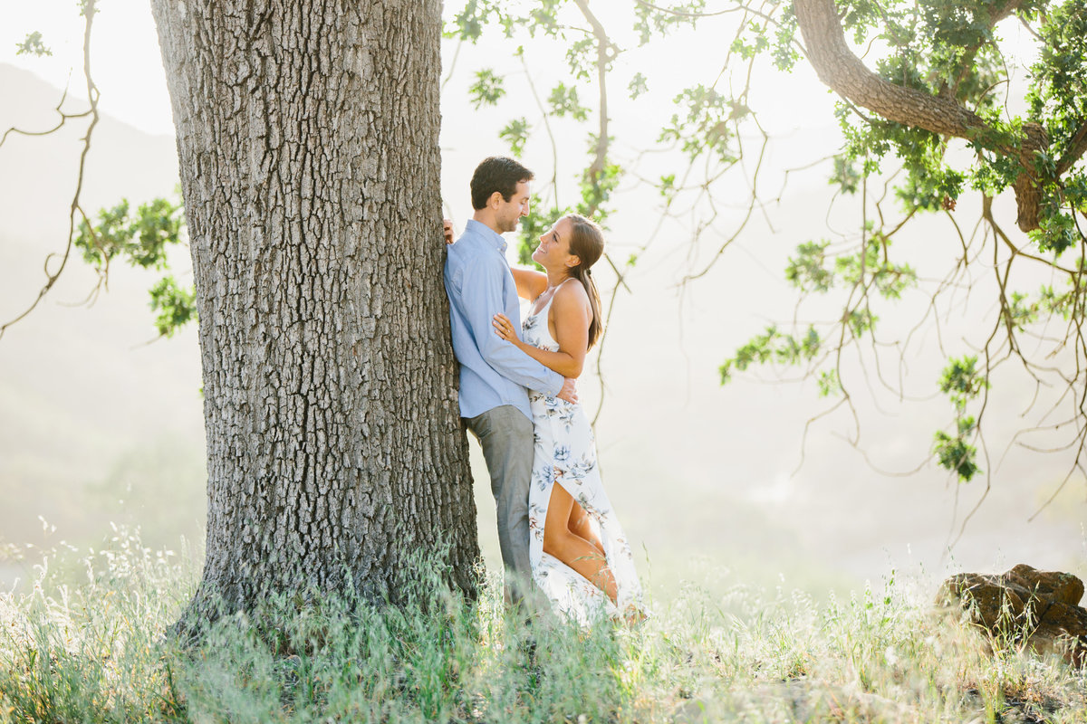 A couple at their engagement session against a big oak tree