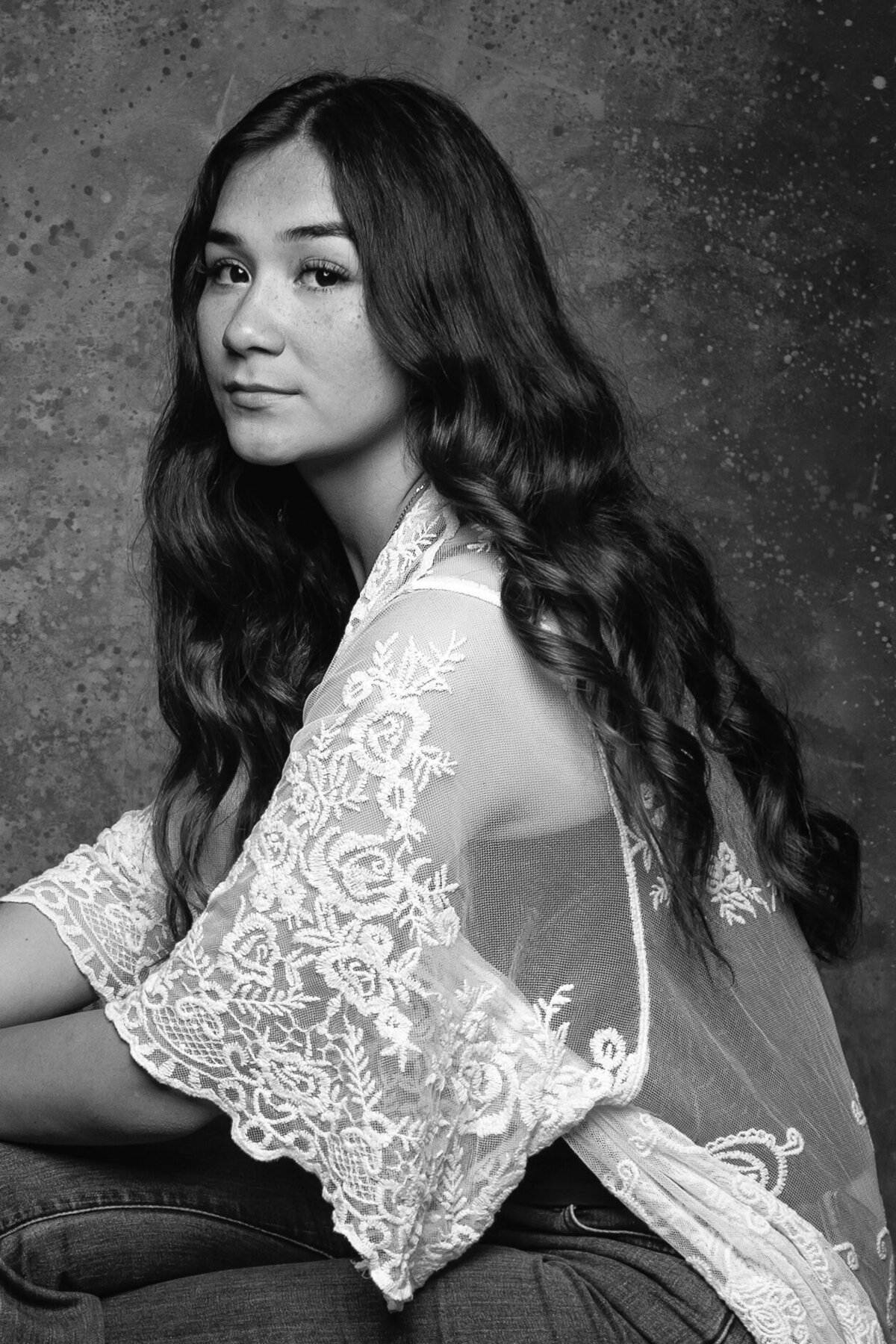 girl in a white lace jacket seated sideways in studio