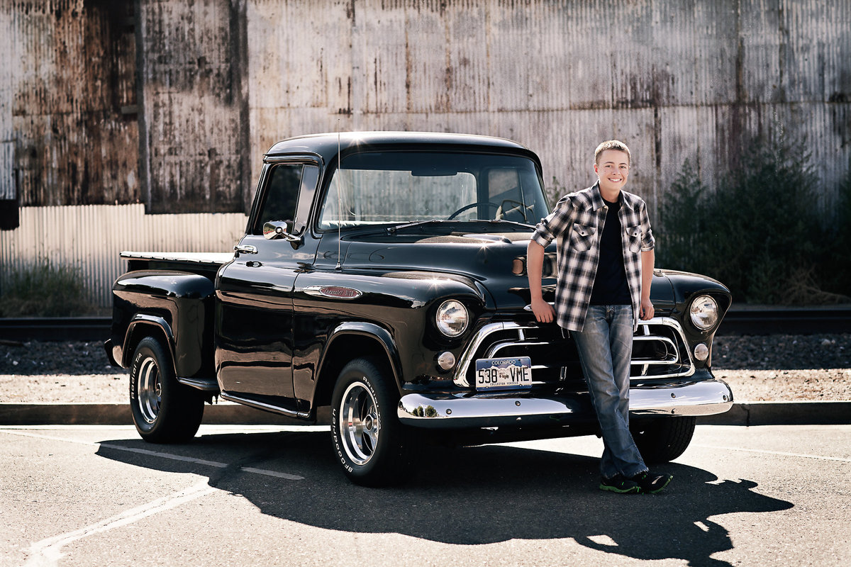 Cool high school guy leans against his black vintage truck during his senior photo shoot