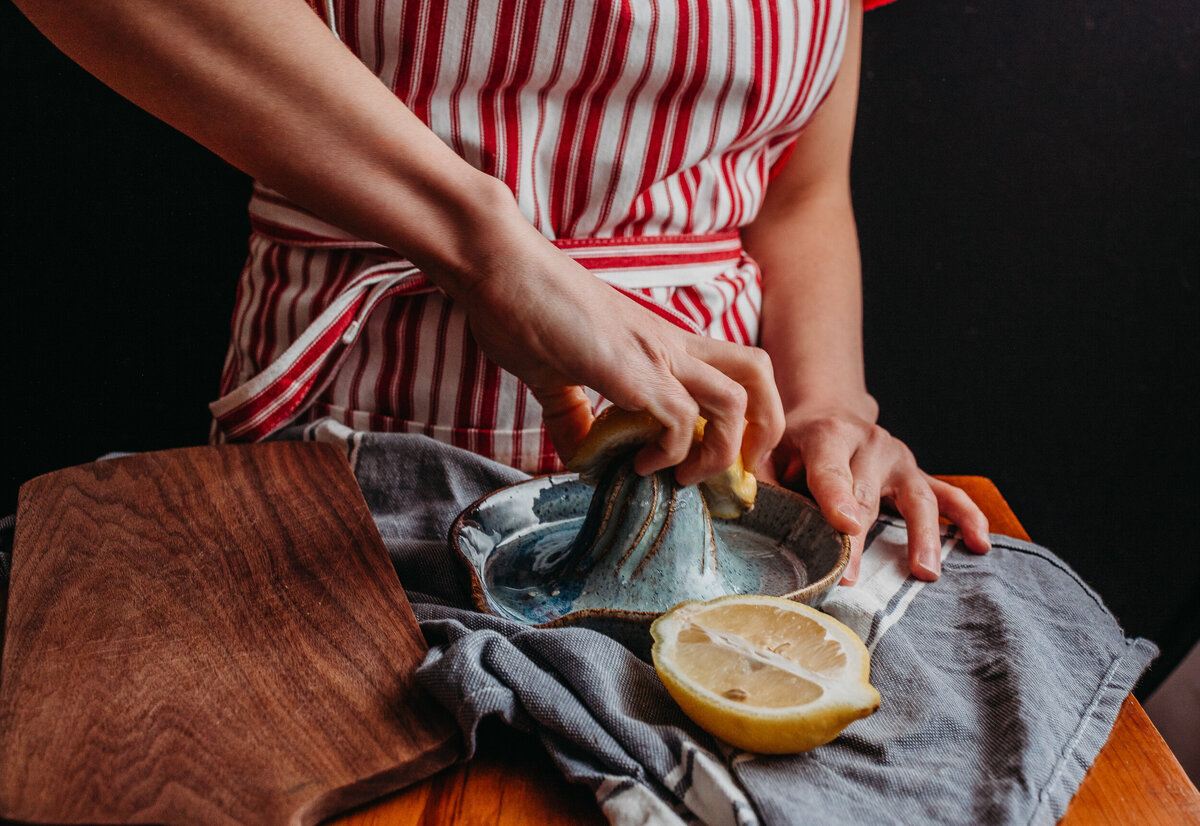 woman wearing red striped apron juices lemon on stoneware