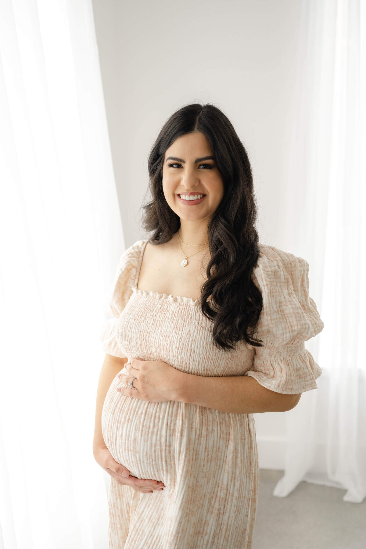 Mother to be with a beautiful smile wearing a pink smocked maternity dress in an Oklahoma City Maternity Photography Studio