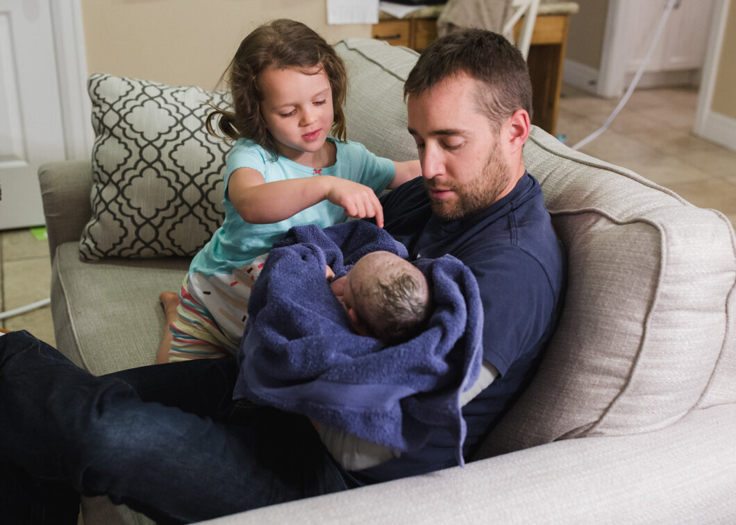 A father and sister meet their new baby at home.