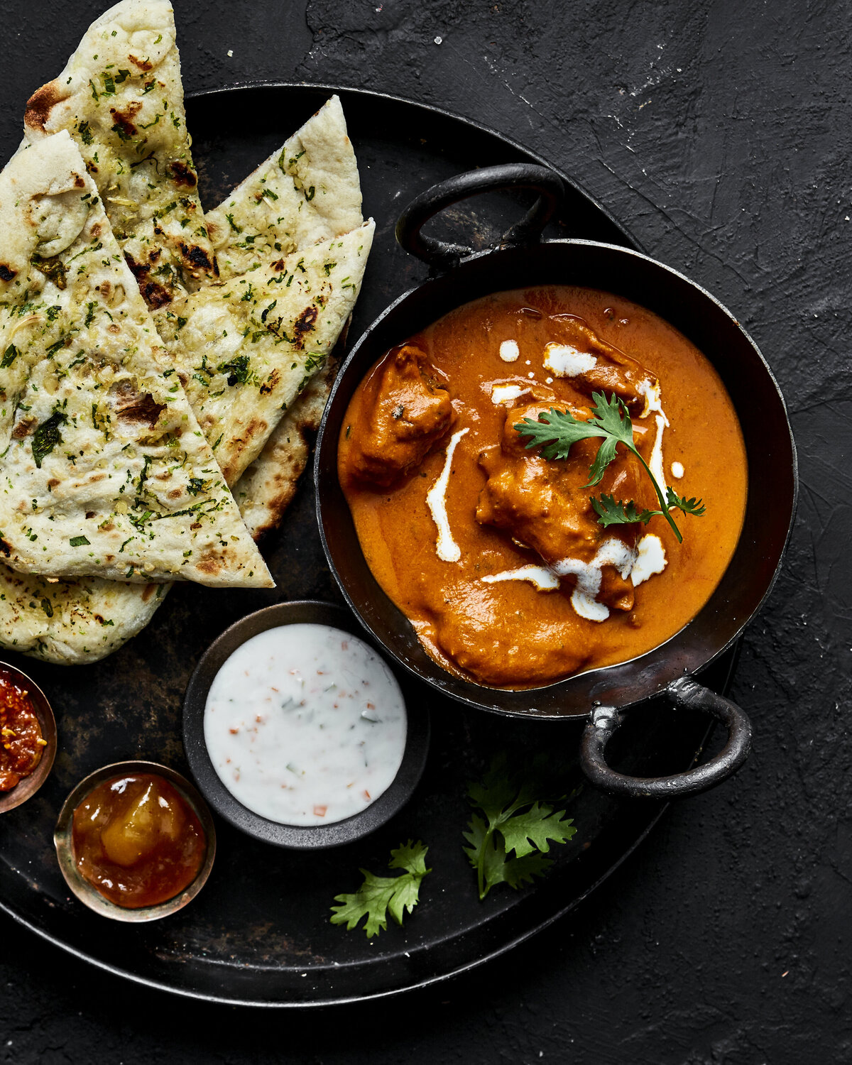 A bowl of butter chicken with naan bread next to them.