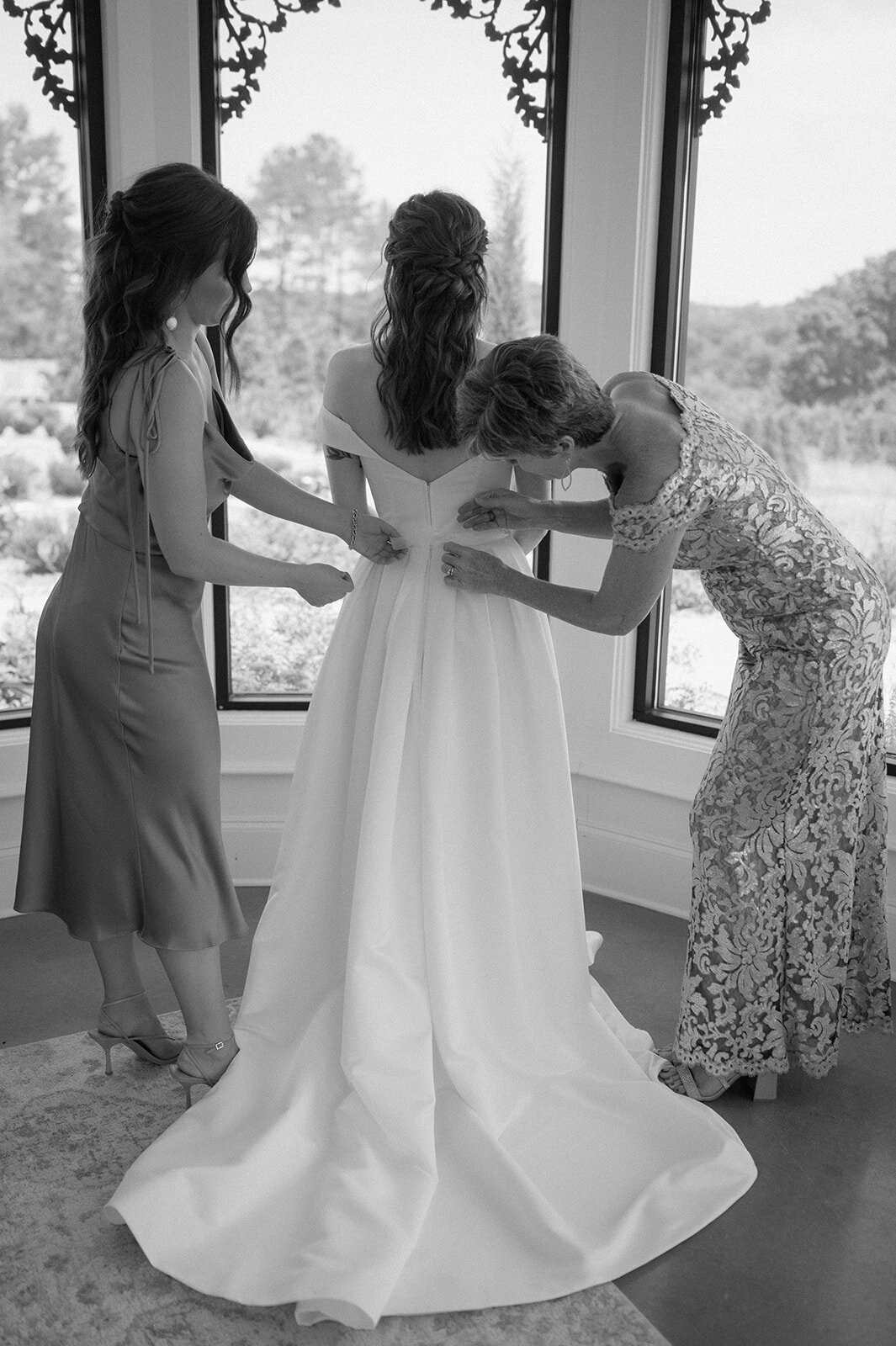 brides mom and sister helping bride get her wedding dress on