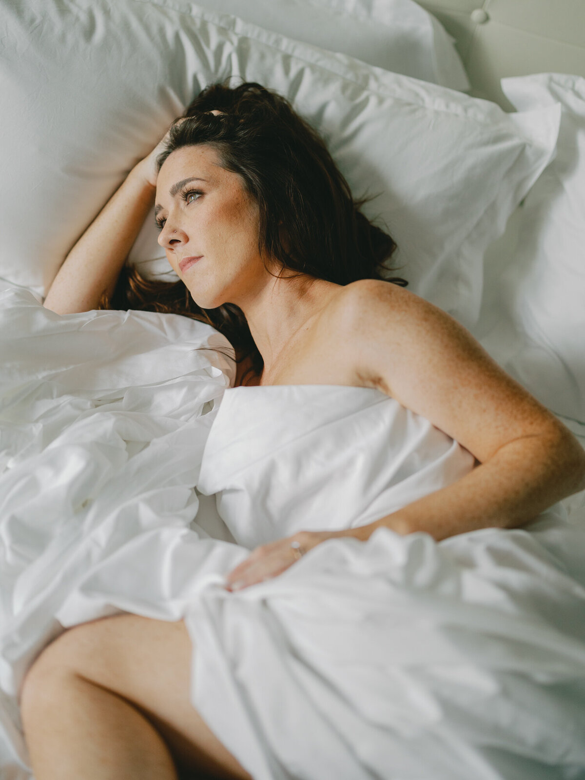 A woman wraps herself in bed sheets as she poses for a boudoir photo