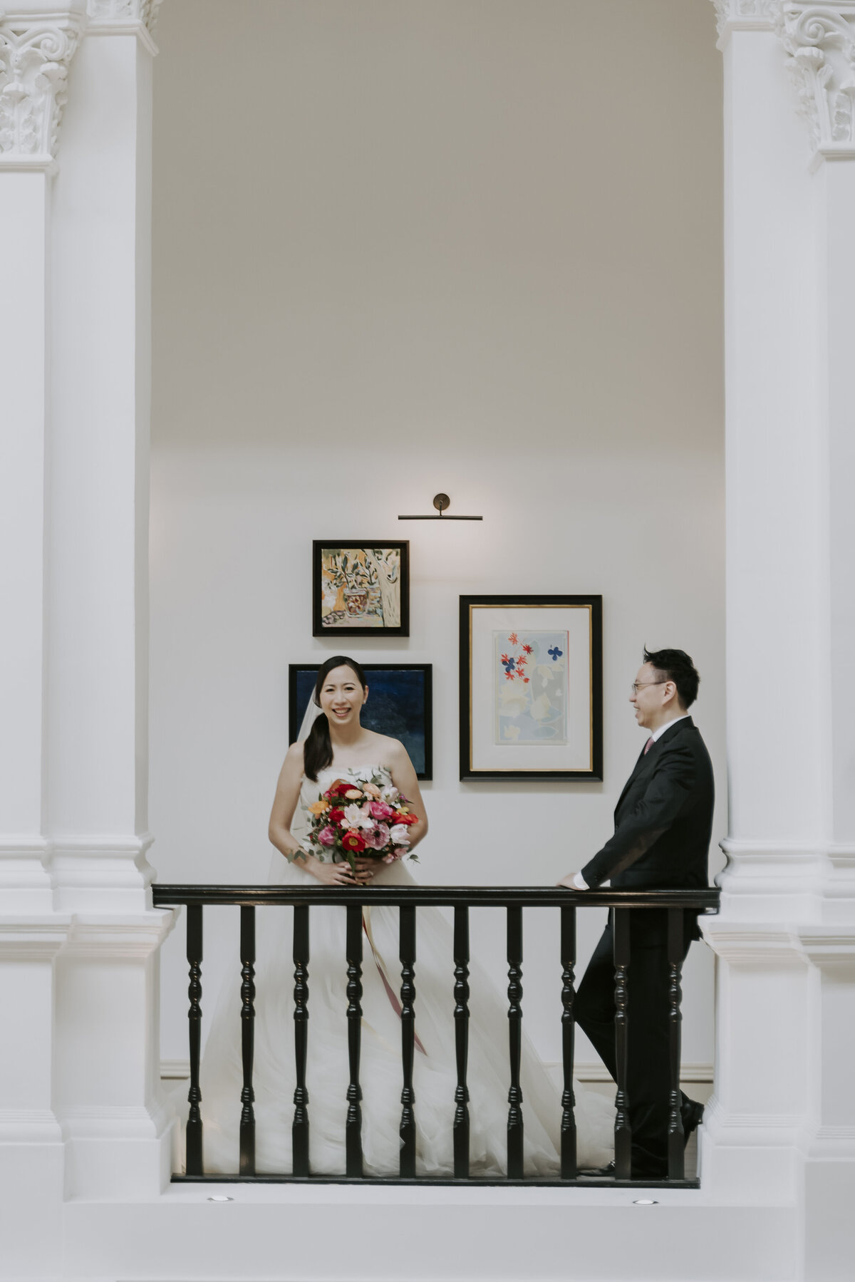 bride wearing a wedding dress and groom wearing a black suit stand in front of artwork at the Raffles hotel