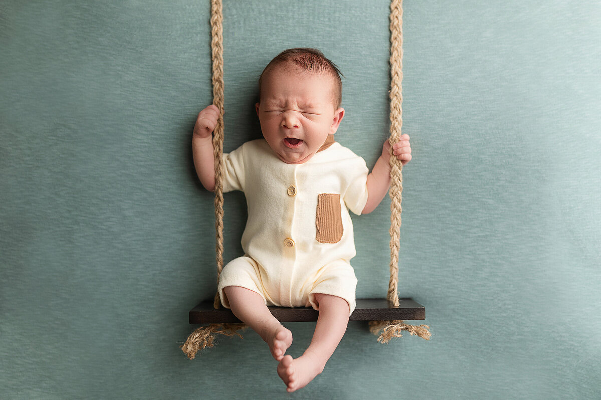 Baby boy on a swing yawning during his newborn session in Southern Minnesota.