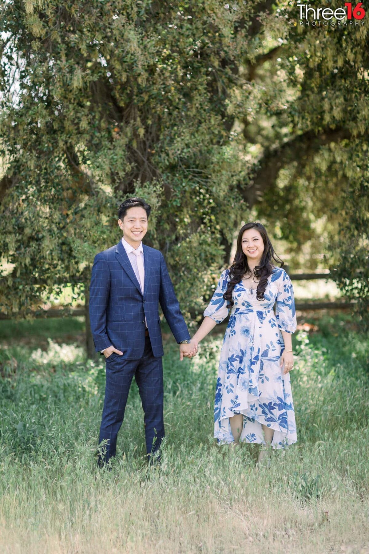 Engaged couple stand under the trees holding hands
