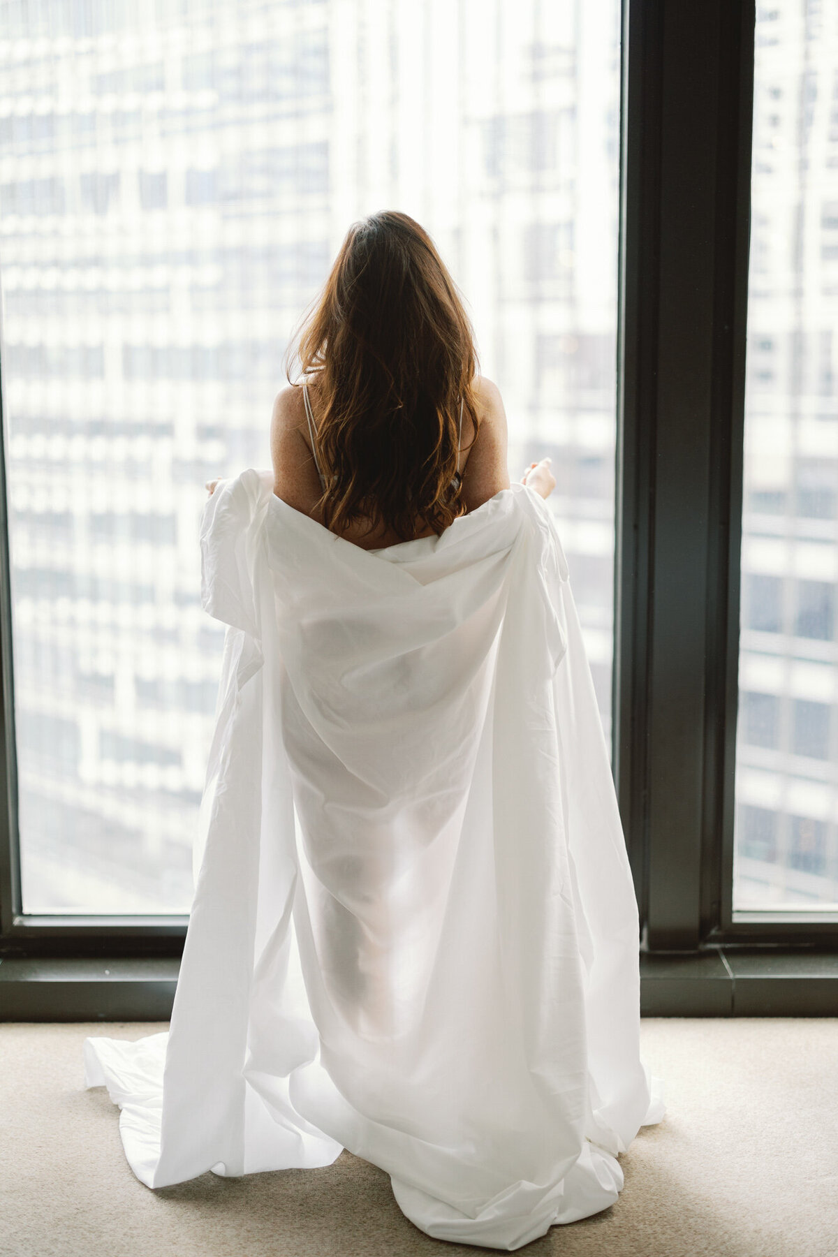 A woman wears bed sheets as she poses for a boudoir photo in downtown Chicago