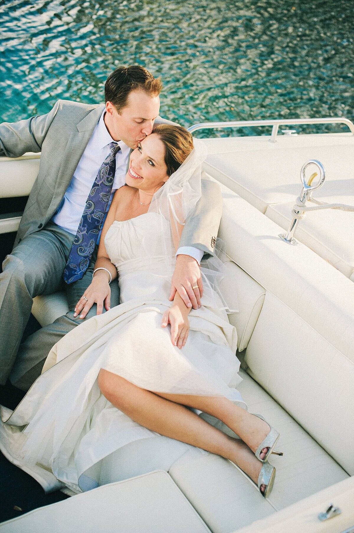 groom kissing his bride on temple as they are sitting in back of a boat in Lake tahoe