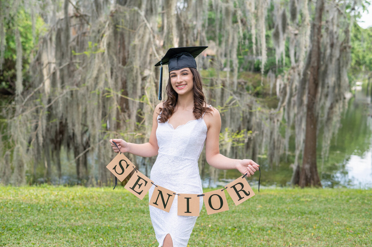 High school senior girl wearing cap holding a "Senior" banner.