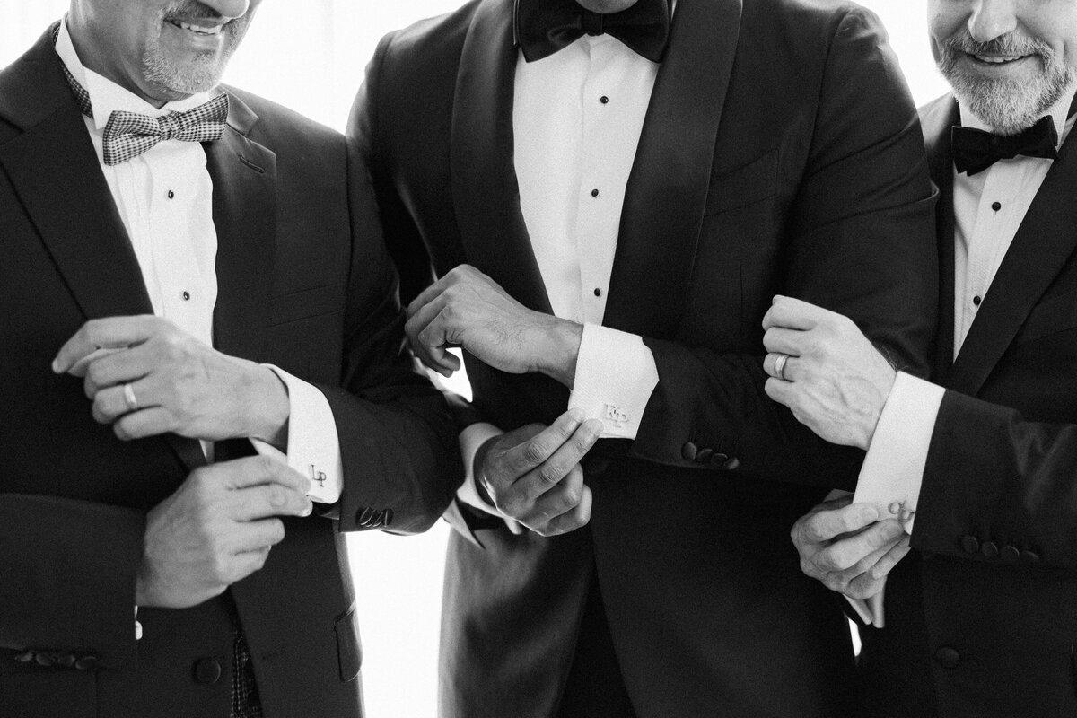A groom stands with his father and father in law  while they show off their matching customized cuff links