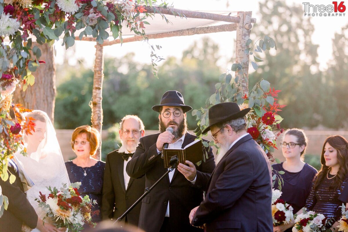 Traditional Jewish reading is being read by a gentleman at the altar as the Rabbi, Bride and Groom look on