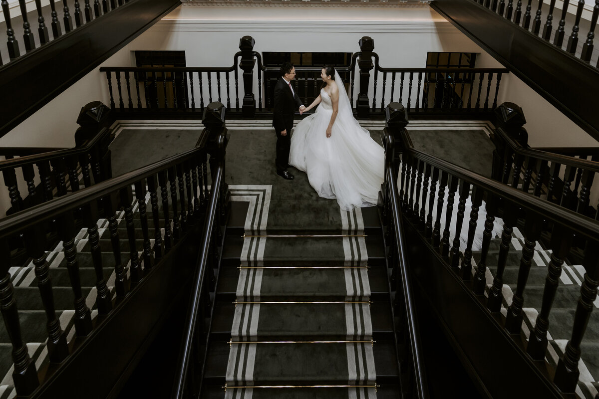 bride and groom holding hands on the staircase in the raffles hotel