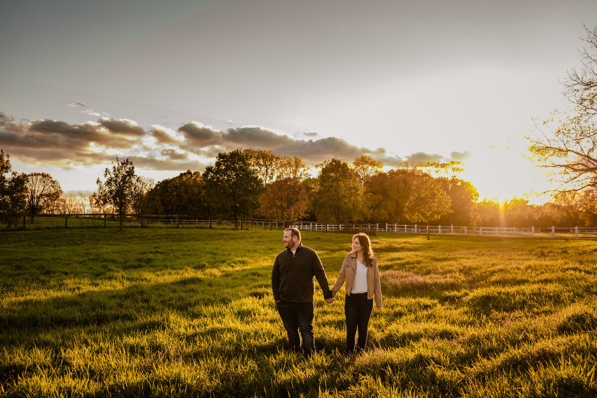 A couple holds hand in a field while the sun sets