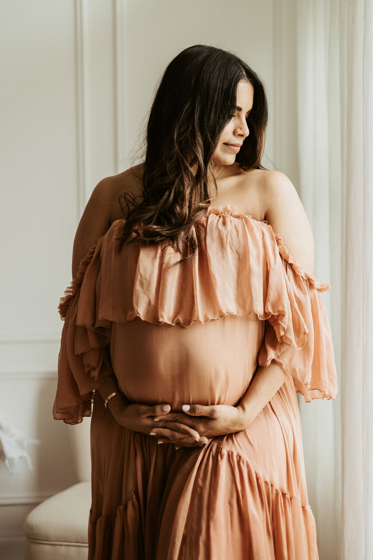 Sweet pregnant mama cradling her baby bump with both hands and looking over her shoulder