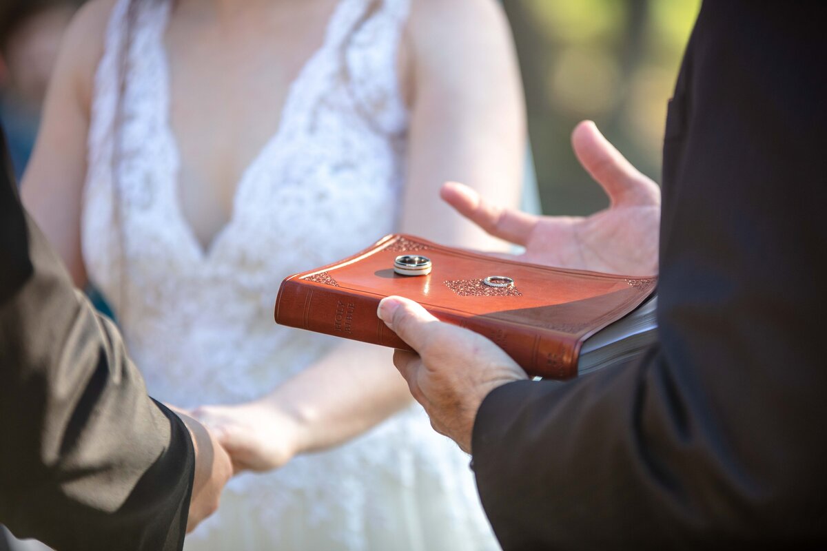 pastor holds bible with rings on top in sunlight at wedding in New Braunfels Texas while couple holds hands