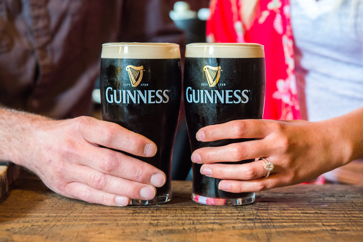 Close-up of a couples hands with engagement ring holding onto pints of Guinness
