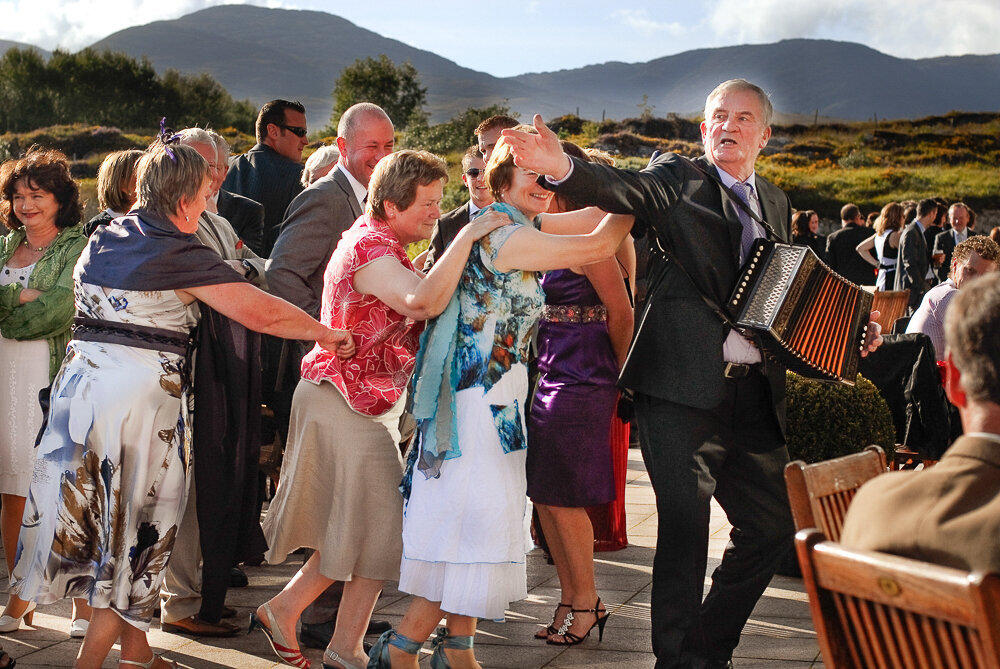 guests doing a dance train on the terrace of the Sneem Hotel while a man plays an accordian