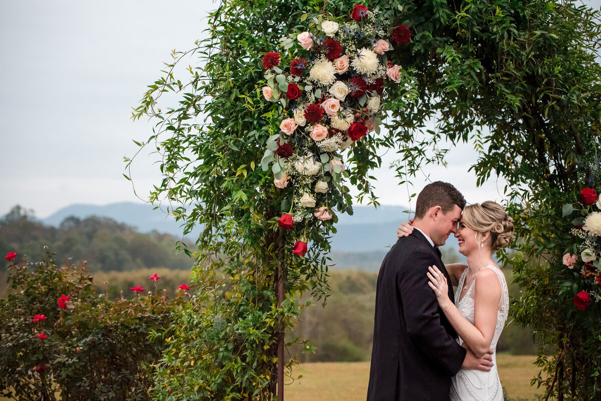 Bride-and-groom-nuzzle-foreheads-under-outdoor-arbor-of-roses-at-the-Pavilion-at-Silver-Fork-Winery