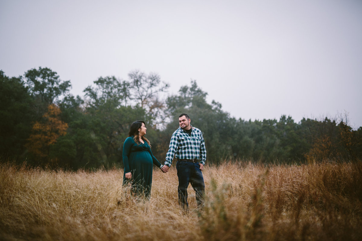 Pregnant couple holding hands in a grassy field for their maternity photography session in San Antonio.