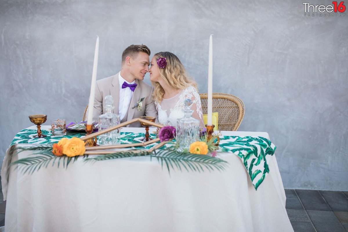 Newly married couple lean in for a kiss while sitting at the sweetheart table