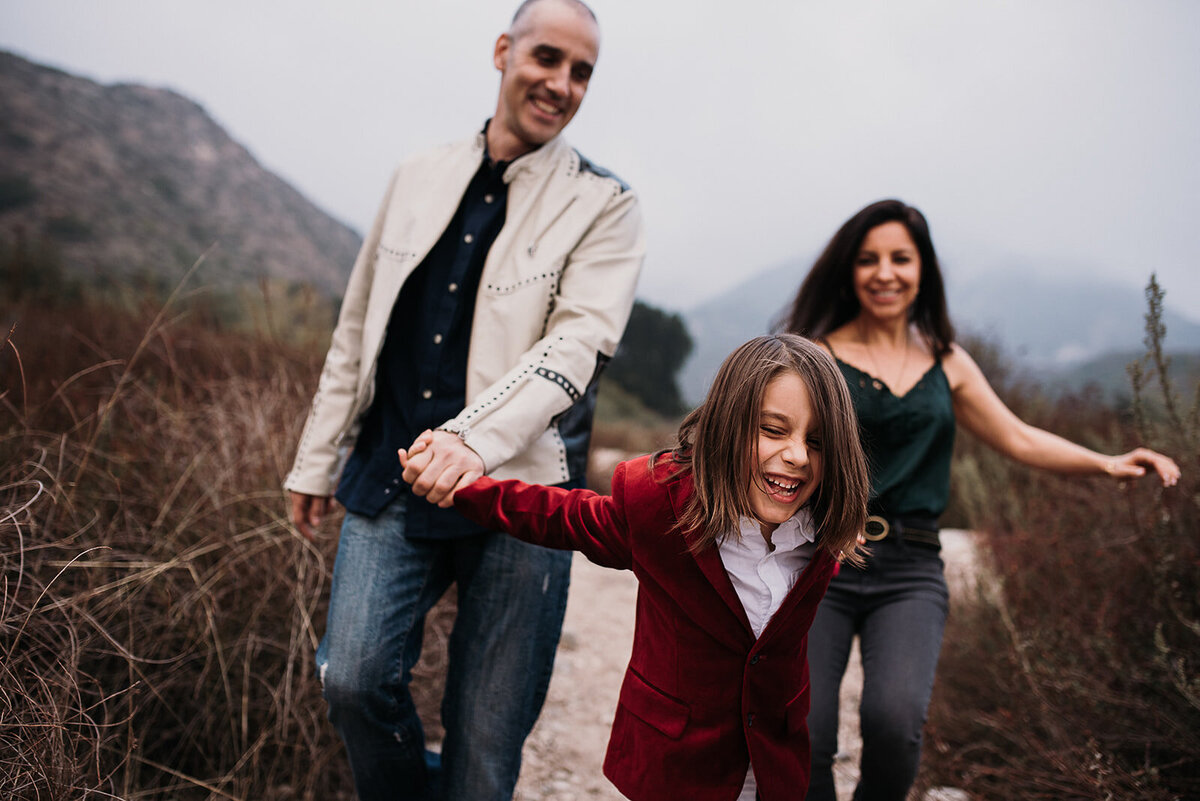 Little boy with long hair pulls laughing parents down hill