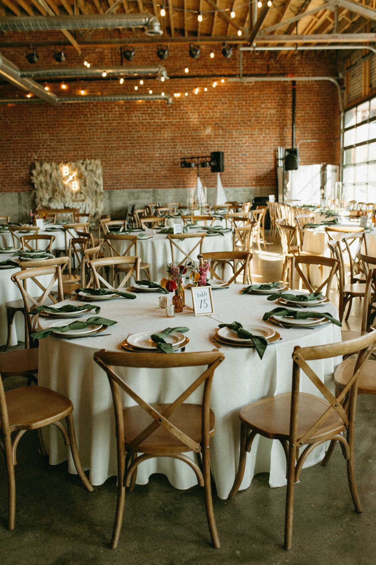 Rustic wedding reception setup in a brick-walled venue with wooden tables, cross-back chairs, and string lights overhead, coordinated by a top wedding planner from Des Moines.