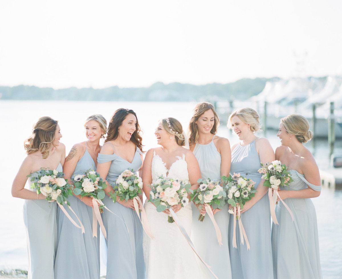 Bride and bridesmaids laugh on dock
