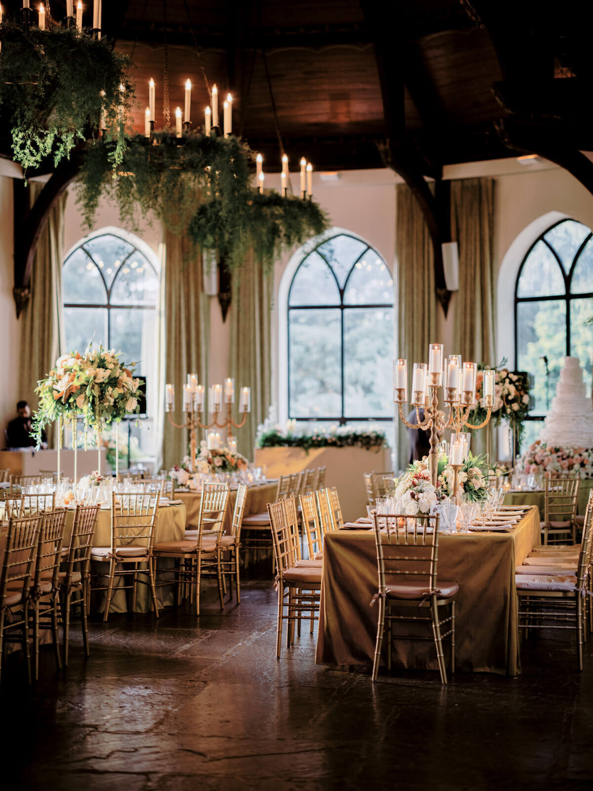 Elegant wedding reception room with chandeliers and bronze tables and chairs with large flower bouquet and candle centerpieces.