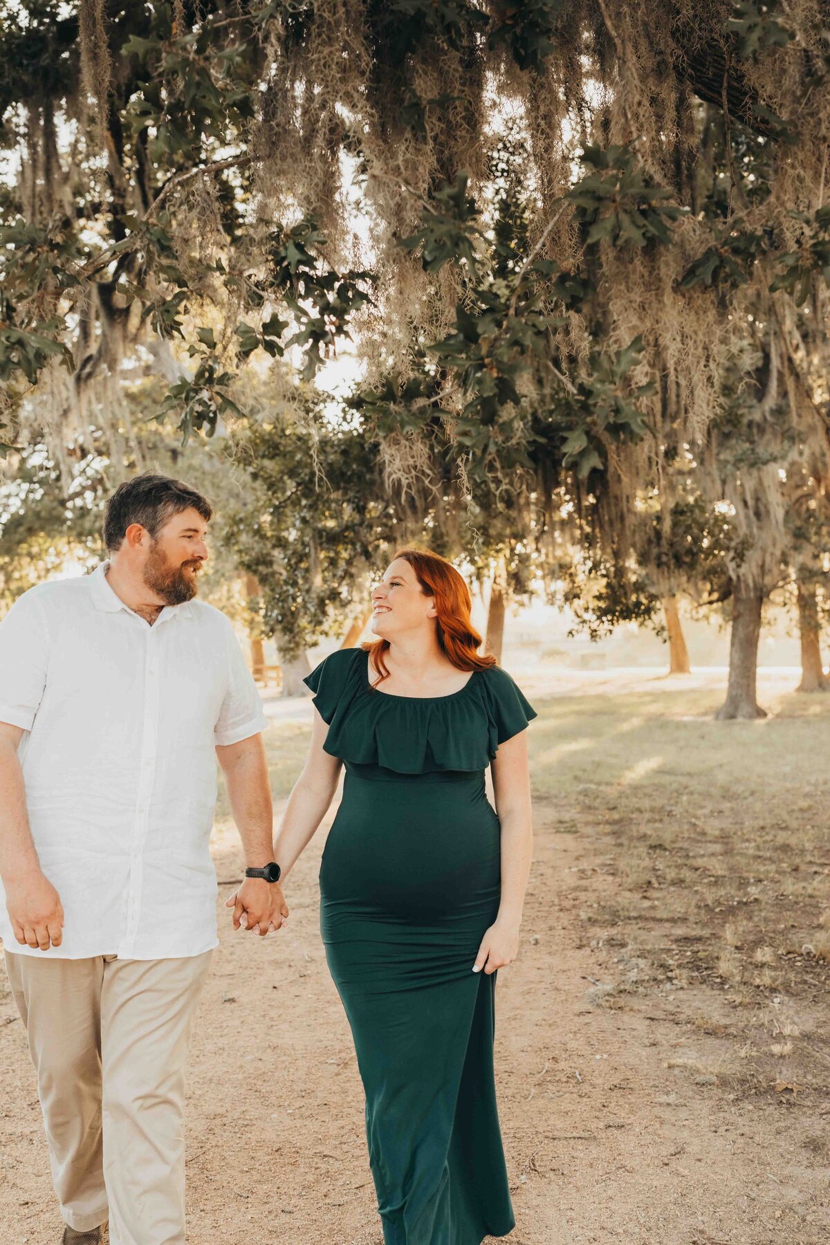 man and wife hold hands while walking down a gravel pathway in Houston, for their maternity pictures.