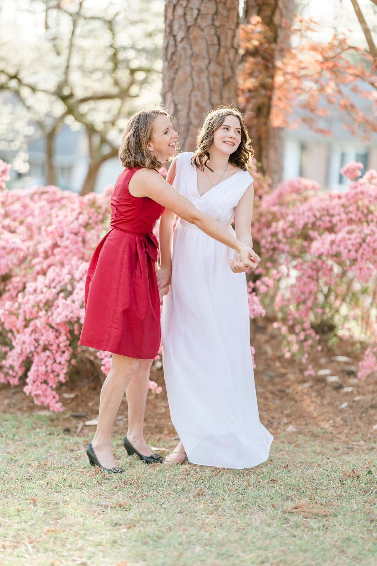 mother and daughter in dresses holding hands looking off in the distance surrounded by cherry blossoms