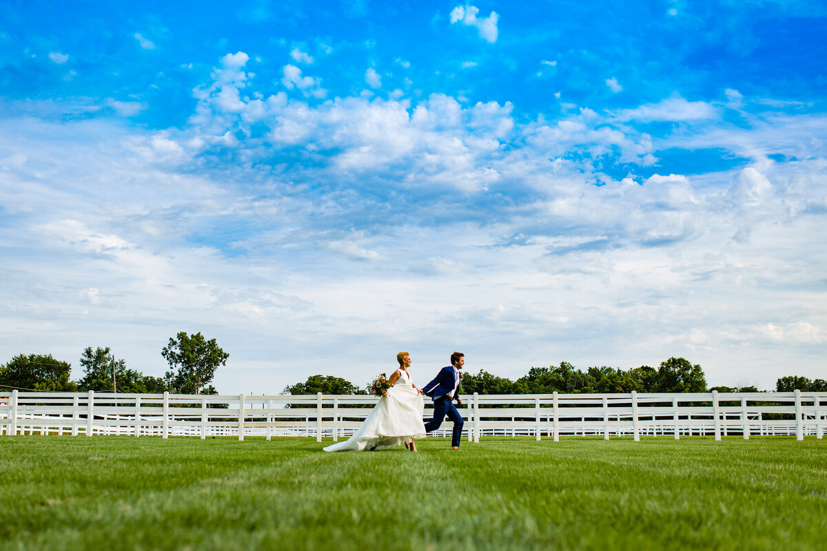 A bride and groom running through a field holding hands. Photo by Adore WEdding Photography