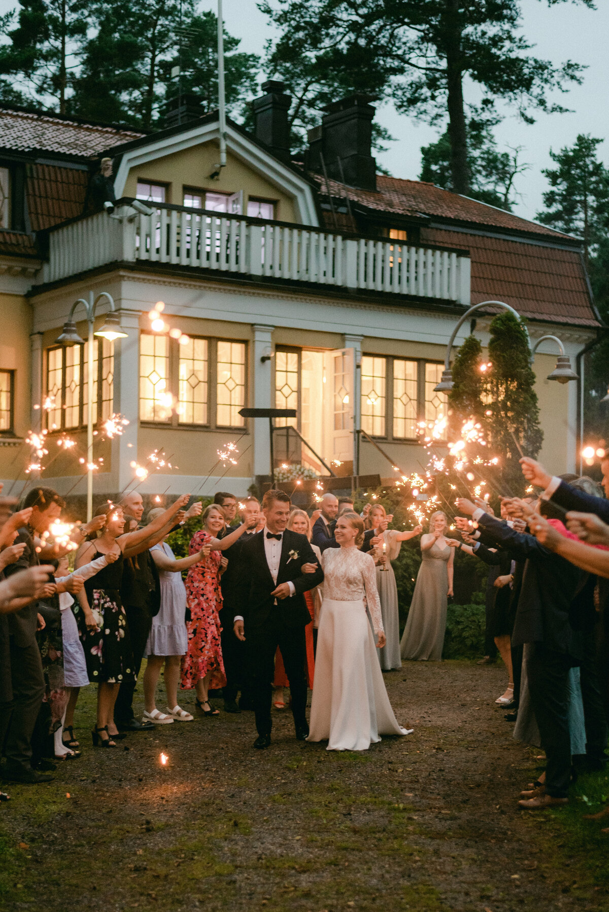 Documentary wedding photo of bride and groom in front of Airisniemi manor in Turku. Wedding guests are holding sparkles. A cheerful and romantic image by wedding photographer Hannika Gabrielsson.