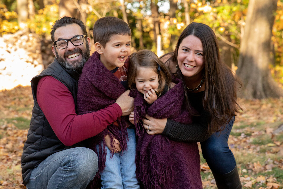 A family of four with two young kids laughs and cuddles in a fall mini-session Nanuet photographer  Milestone Images