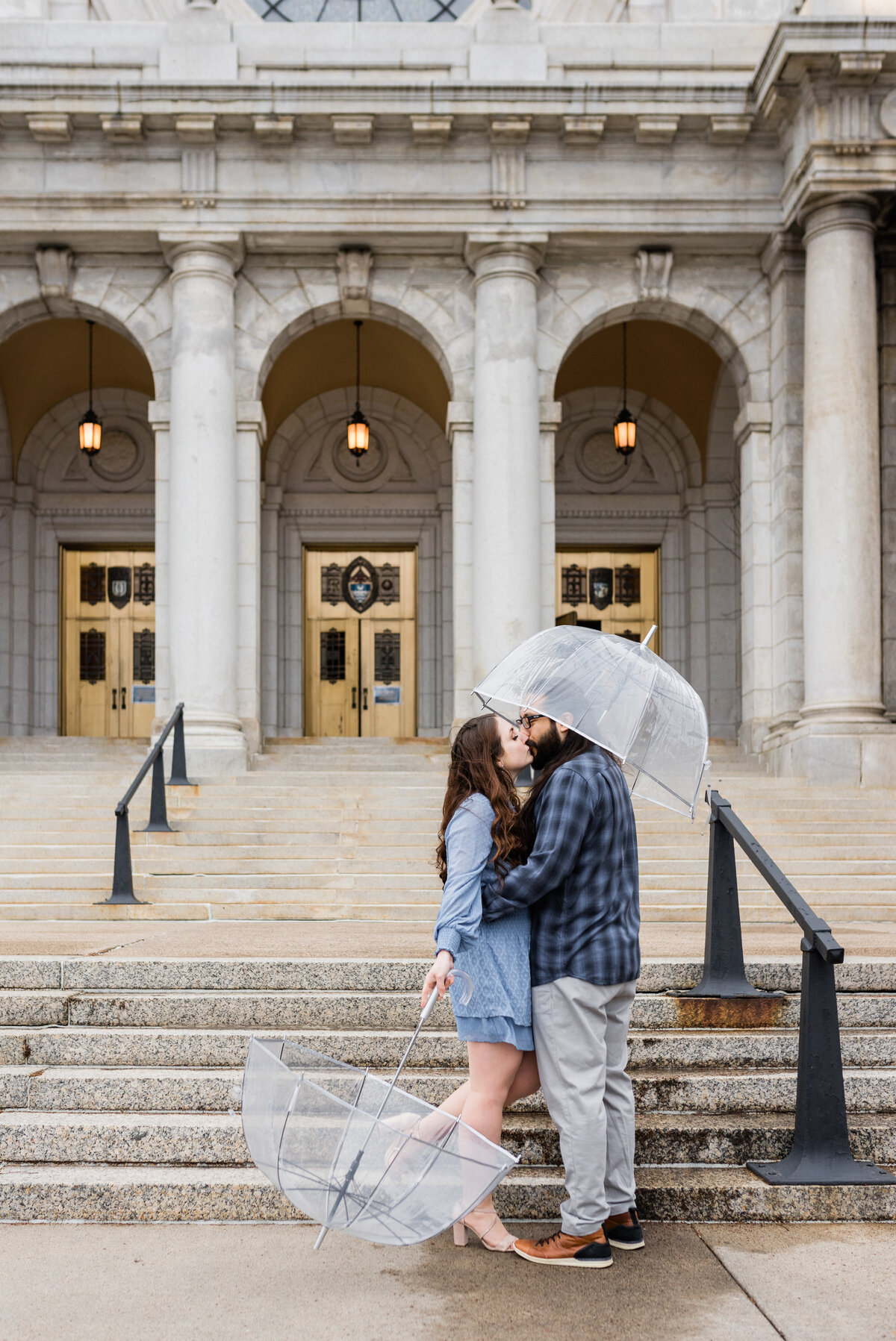 Couple kissing with one umbrella up and one umbrella down in front of church