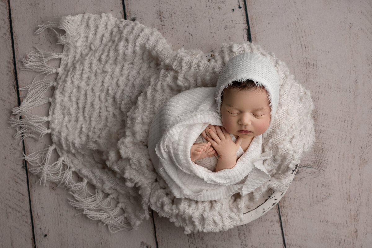 Main Line's best newborn photographer, Katie Marshall, captures a swaddled baby sleeping with her hands and toes exposed and folded on her chest. Aerial image.