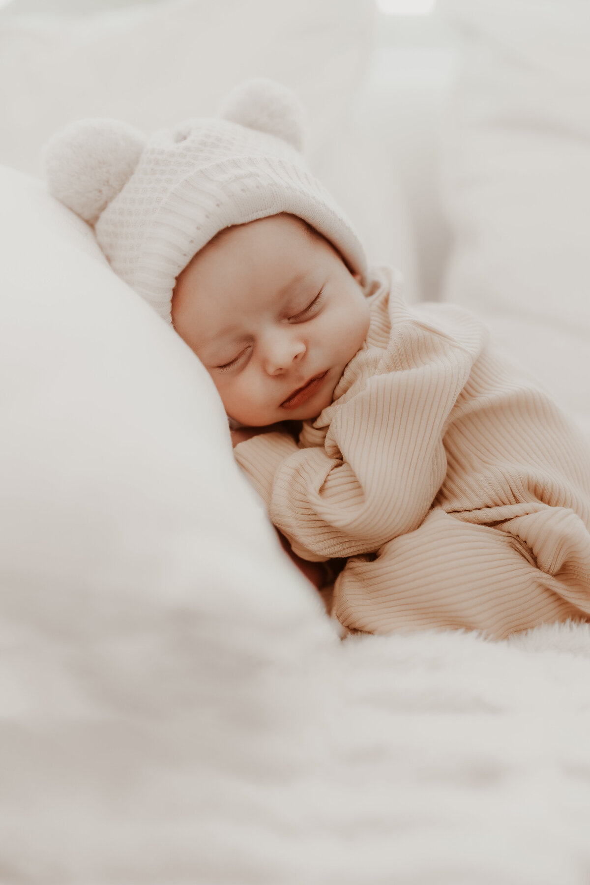 newborn baby boy with white hat laying on pillow for newborn session in denver