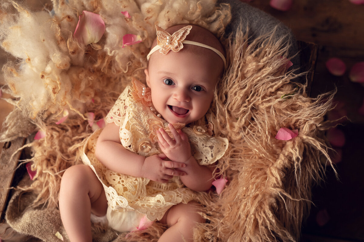 A baby girl gives a huge grin to the camera while laying in a furry blanket nest in our Waukesha portrait studio.